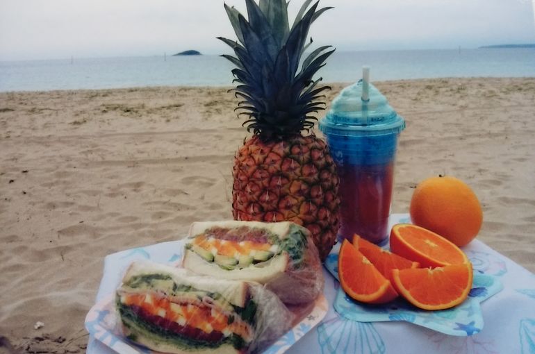 砂浜に置かれたテーブルの上のパイナップル、オレンジ、サンドイッチなど