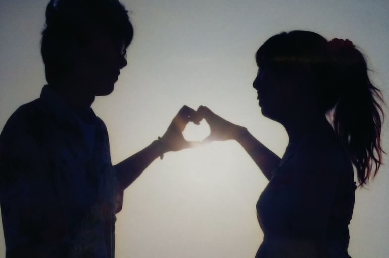 ポニーテールの横顔、二人の手で小さなハートを作っている。