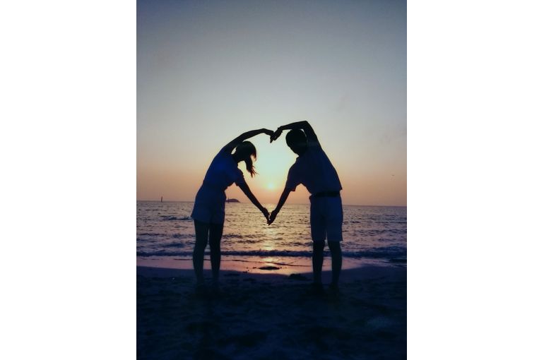 二人の腕をいっぱいに使って大きなハートを作っている。そのハートのなかに夕日が写っている。