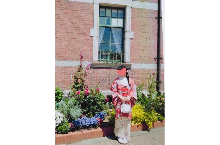 色々な花が咲く花壇の前に立つ着物姿の女性