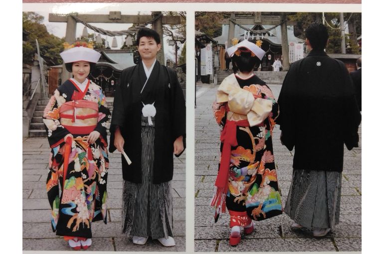 黒本振袖の花嫁がお引きずりの裾をからげて右手で持っている。隣に新郎。正面と後ろ姿の2枚