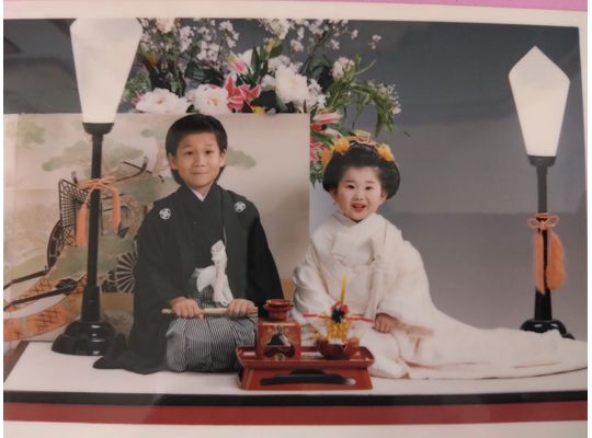 ３歳 白打掛姿の妹(角かくし綿帽子無し)、6歳 黒紋付羽織袴姿の兄、二人かしこまって笑顔