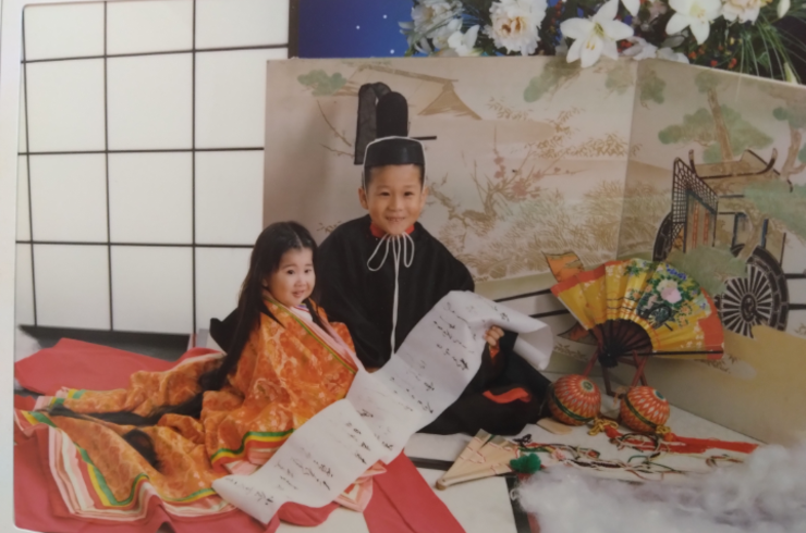 2歳の女の子と5歳の男の子が平安時代の衣装を着て、畳に座って巻紙を持ってニッコリ笑っている。