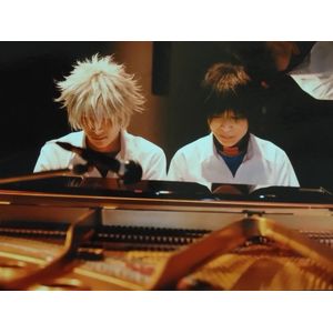 中学校男子夏の制服を着たカヲル役(銀髪)の次男が高音側、シンジ役(黒髪)の母親が低音側に並んで座り演奏する姿をピアノ越しに正面から写している